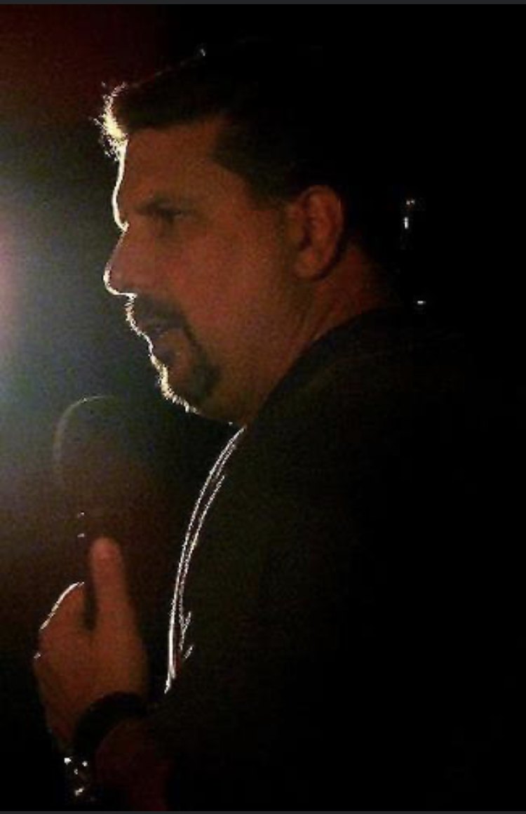 Greg holding a microphone under stage lighting